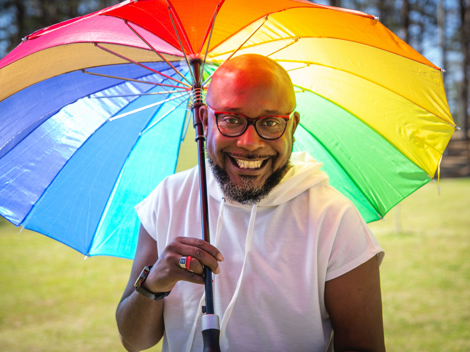 Black man living with HIV in USA smiling and holding a big umbrella with rainbow colours