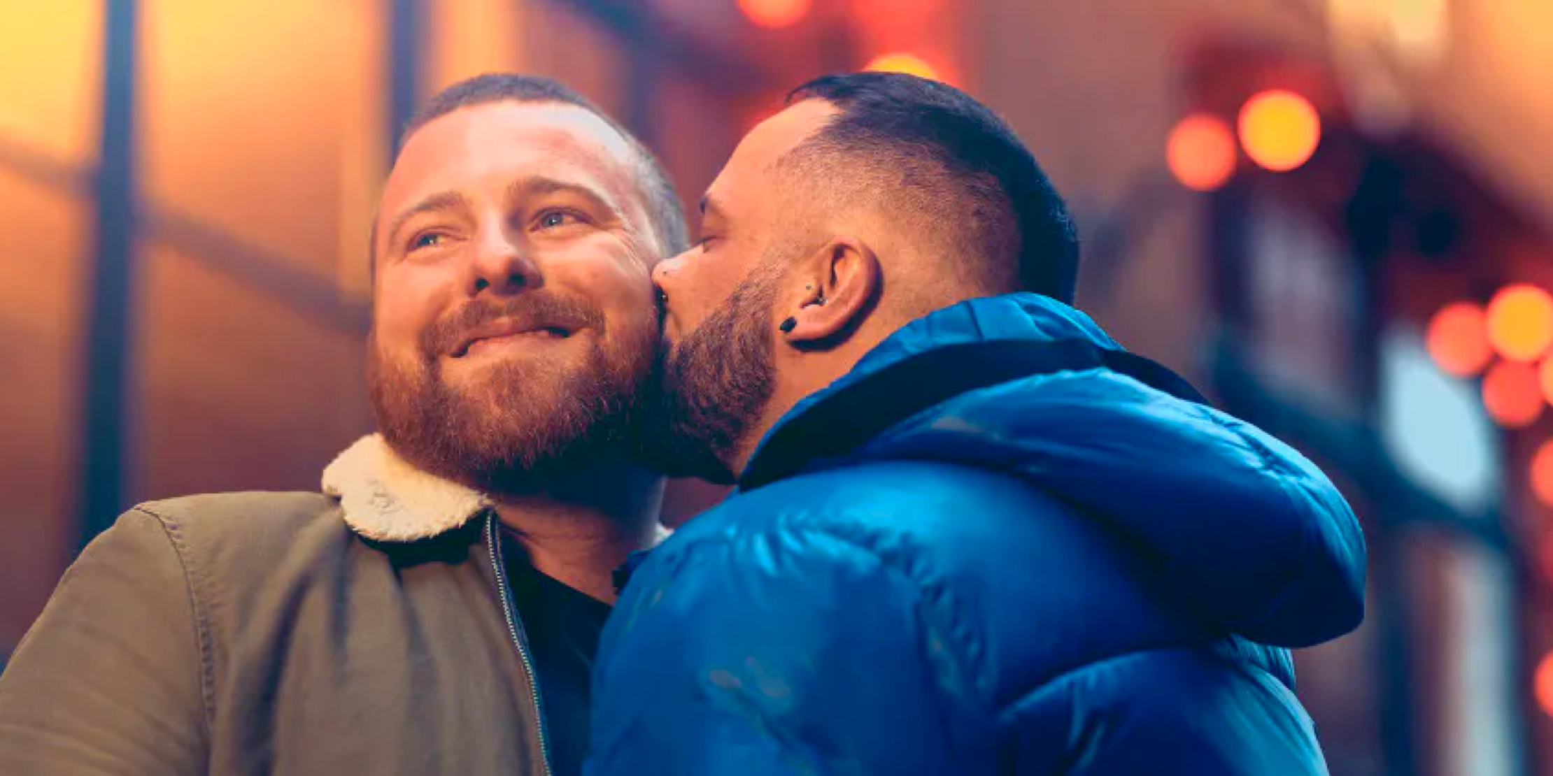 A man smiling as another man kisses his cheek