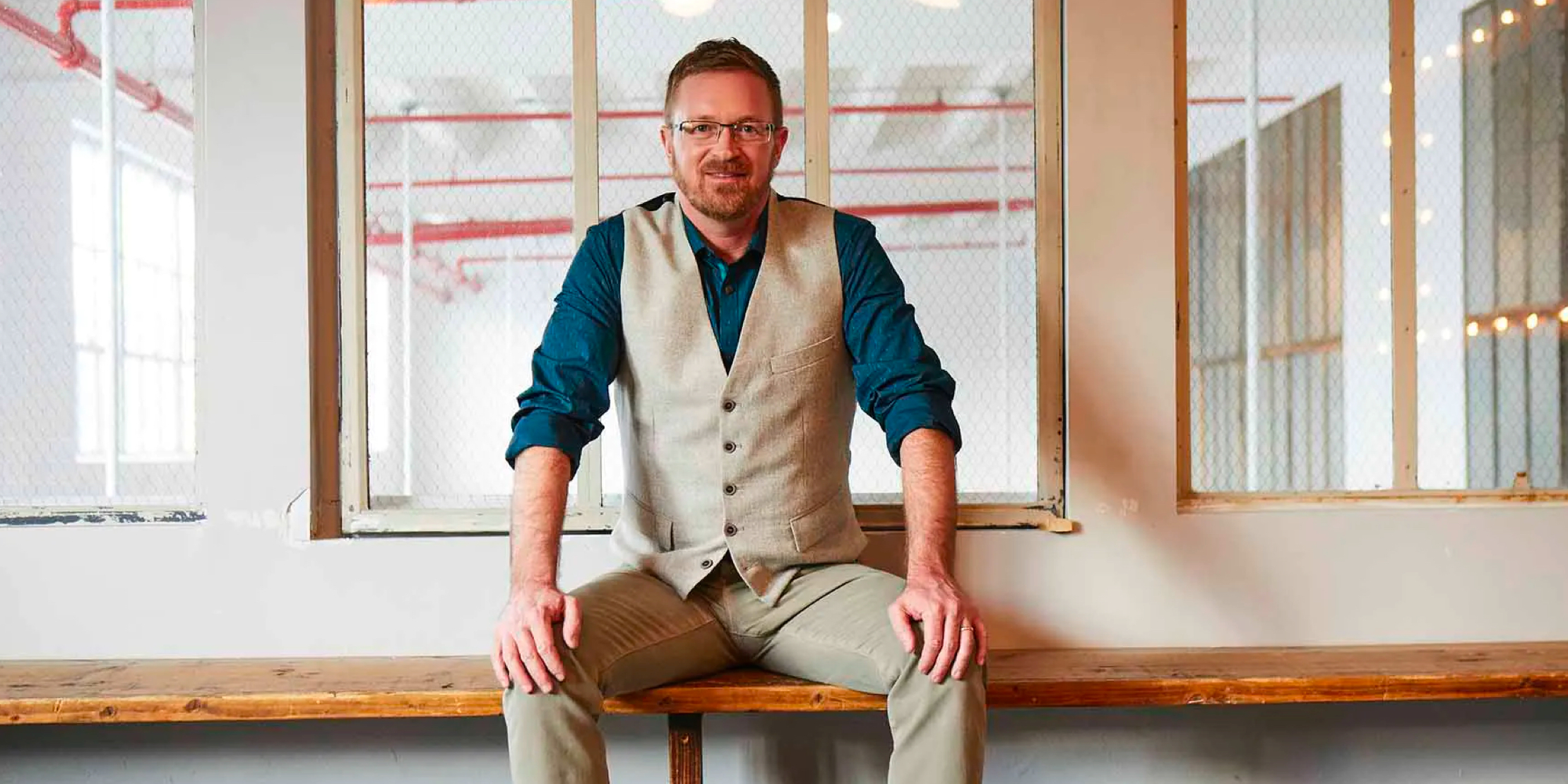 A man sits on a wooden bench and smiles at the camera